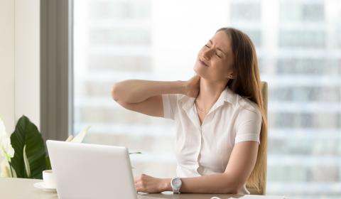 Photographie d'une jeune femme au travail, devant son ordinateur et souffrant de douleurs de la nuque et du dos