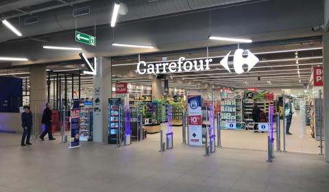 Entrée d'un supermarché Carrefour avec portiques et enseigne lumineuse