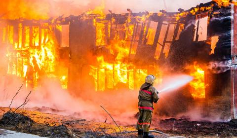 Un pompier en train d'éteindre un grand incendie de maison ou de petit immeuble entièrement ravagé par les flammes