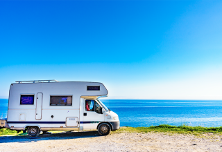 Vue de profil d'un camping car au bord de mer et par un grand ciel bleu