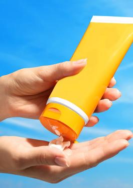 Plan serré sur des mains pressant un tube de crème solaire sur fond de grand ciel bleu d'été
