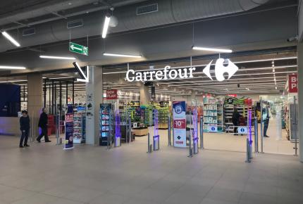 Entrée d'un supermarché Carrefour avec portiques et enseigne lumineuse