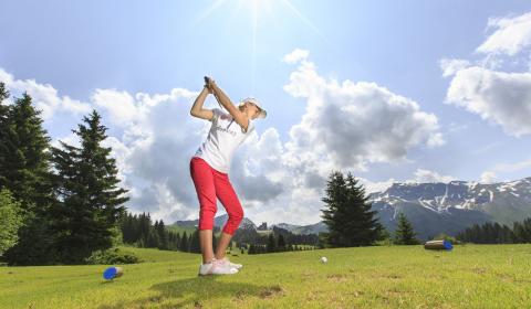 L'été, joueuse de golf en plein swing sur une pelouse avec les cimes des montages d'Avoriaz au loin